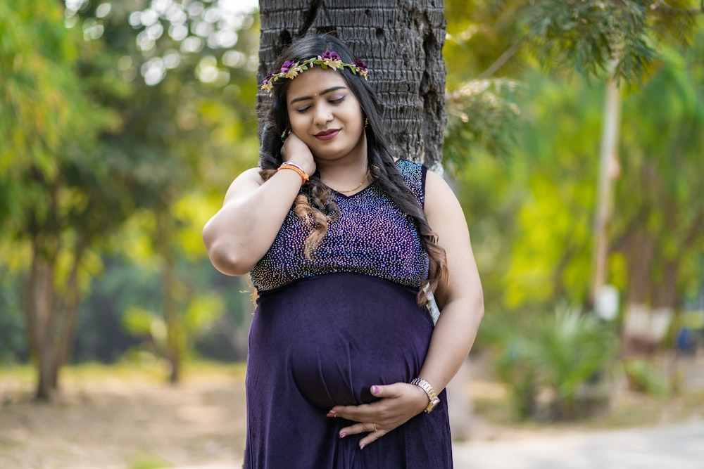 a pregnant woman standing next to a tree