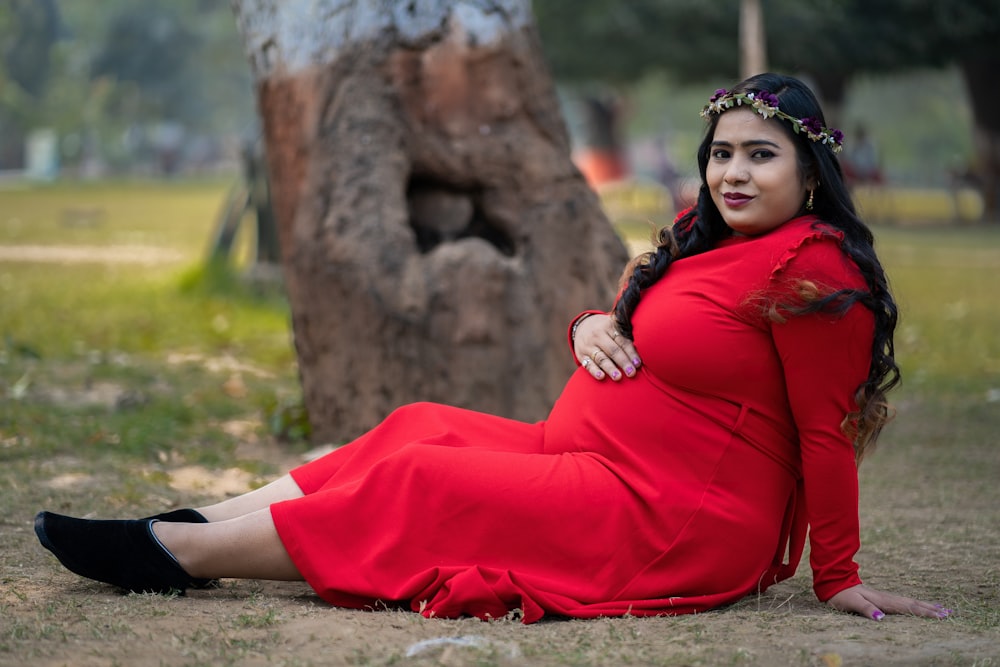 a woman in a red dress sitting next to a tree