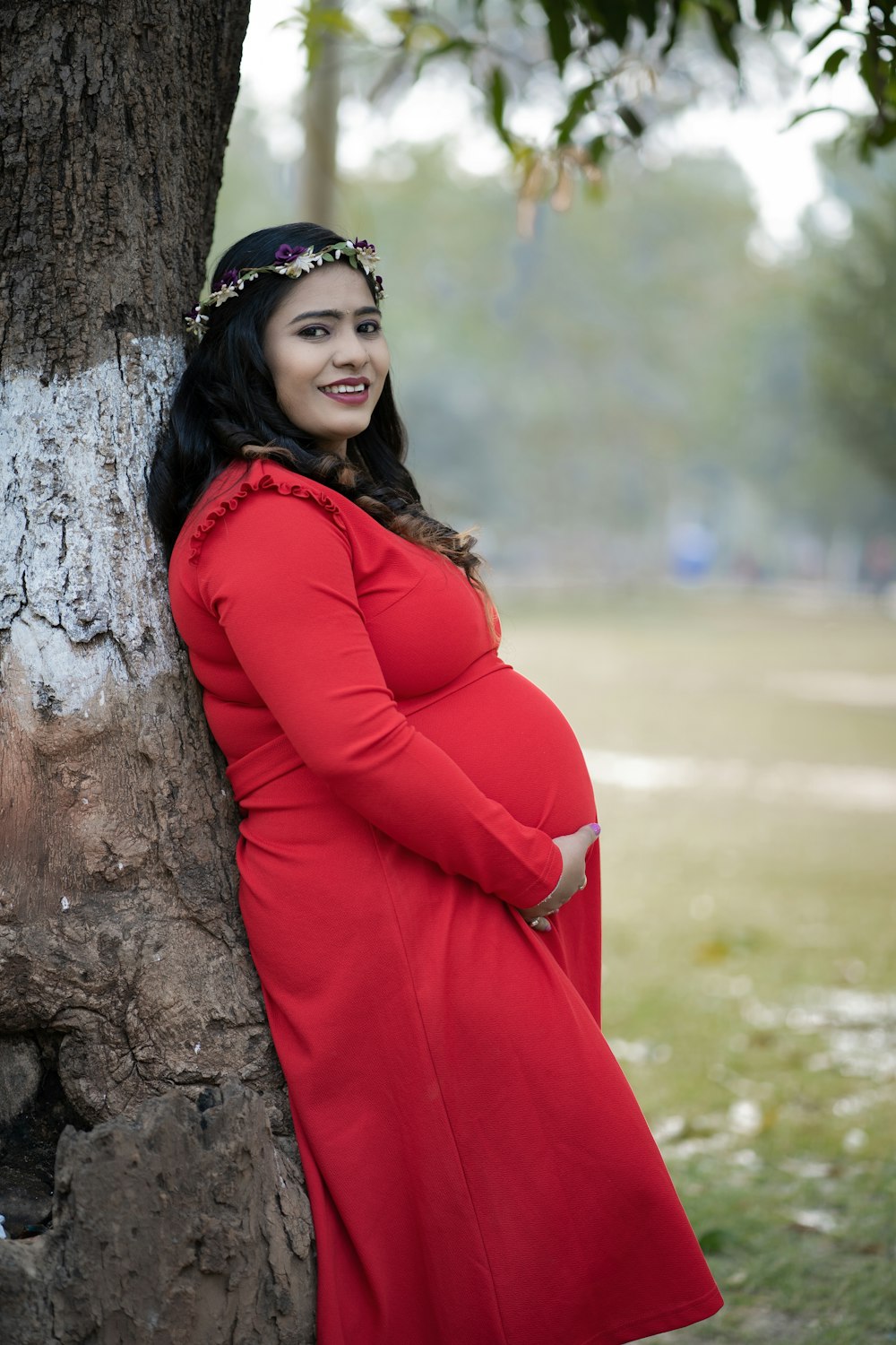 a pregnant woman leaning against a tree in a park
