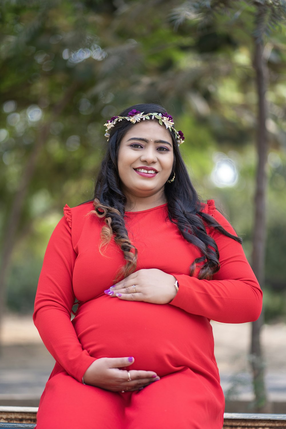 a pregnant woman in a red dress sitting on a bench