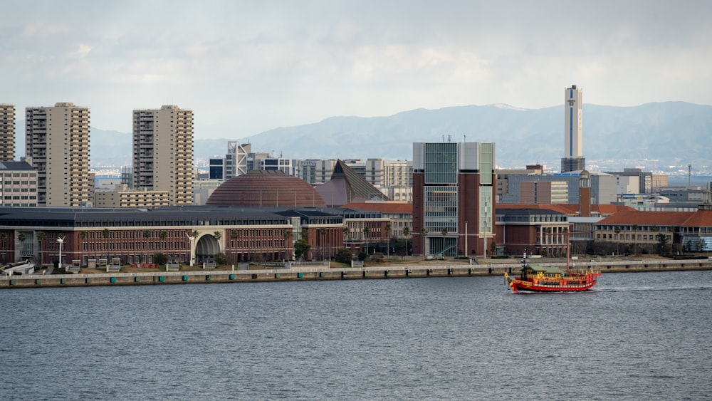 a red boat in a body of water near a city