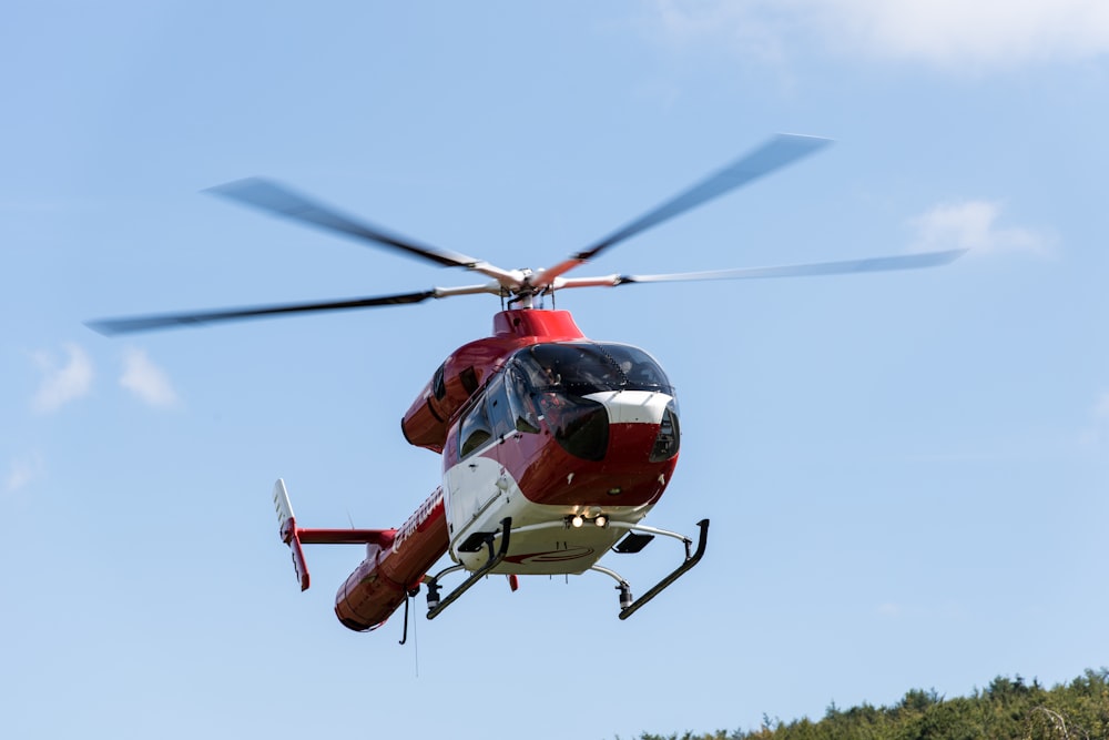 a red and white helicopter flying through a blue sky