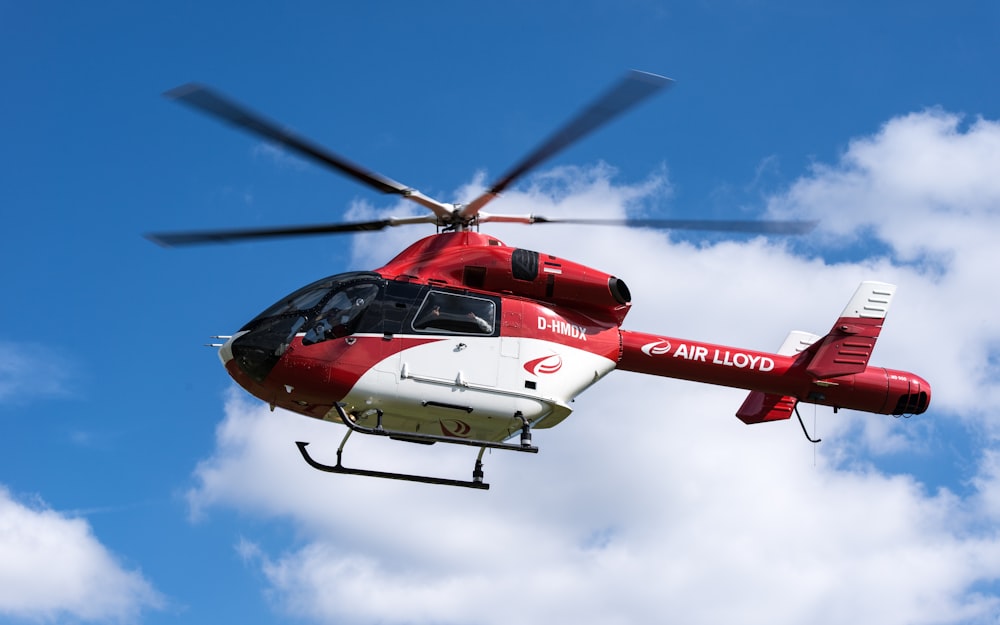 a red and white helicopter flying through a blue sky