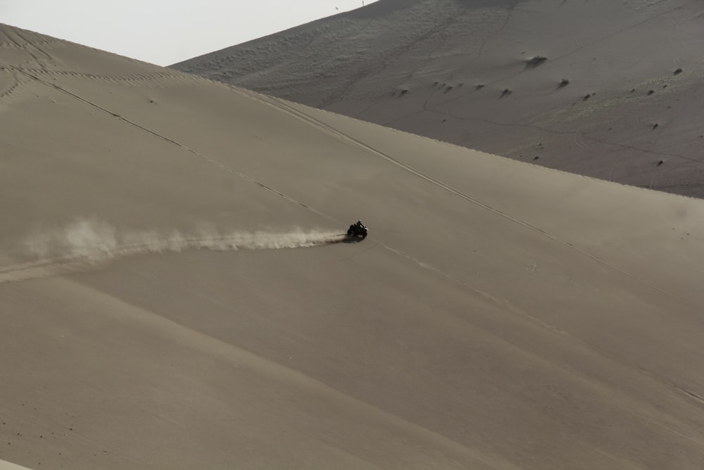 a person riding a motorcycle on top of a sandy hill