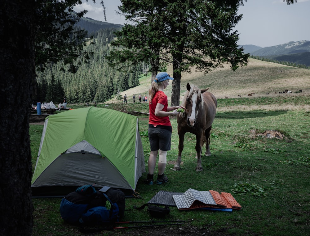 a woman standing next to a tent next to a horse
