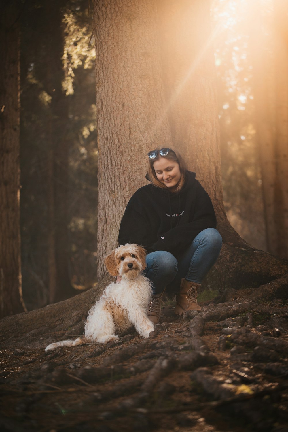 a woman sitting next to a dog in the woods