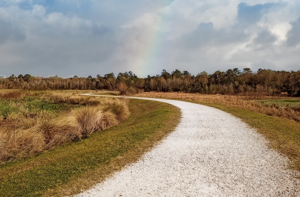 a gravel road with a rainbow in the background