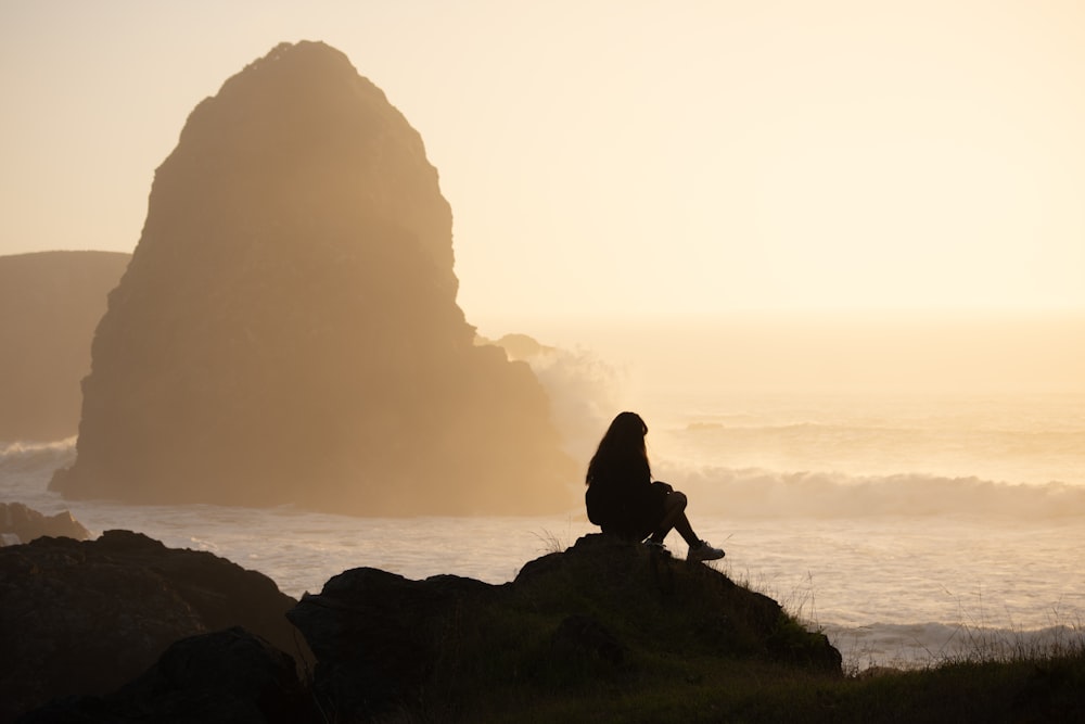 a person sitting on top of a rock near the ocean