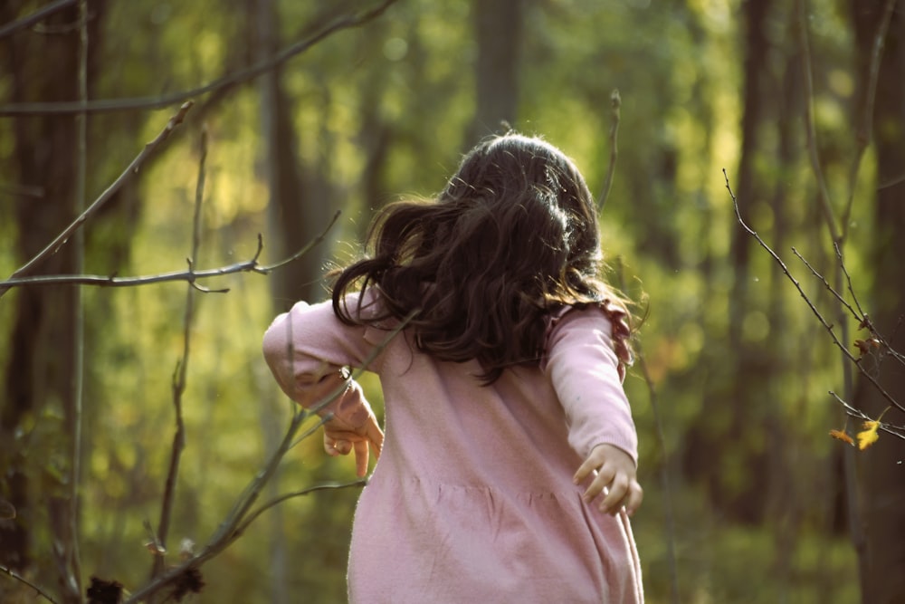 a little girl in a pink dress walking through a forest