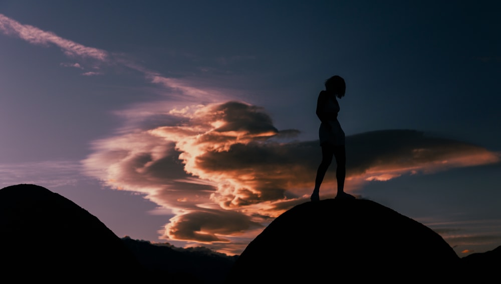 a woman standing on top of a mountain under a cloudy sky