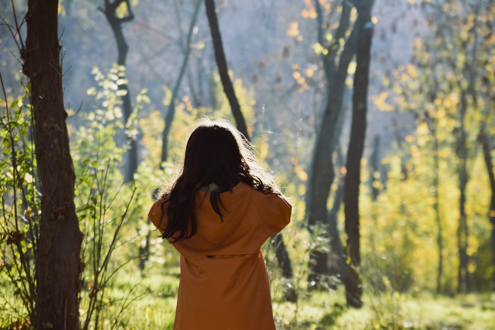 a woman in an orange coat walking through a forest