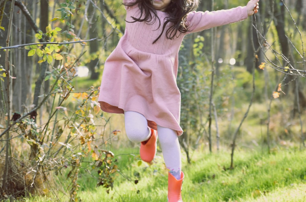 a little girl in a pink dress and hat jumping in the air