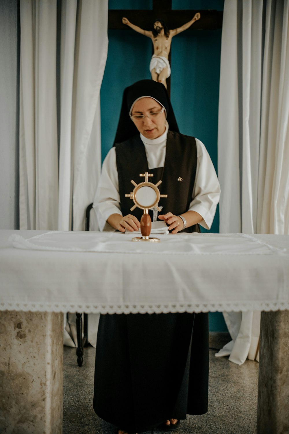 a nun is sitting at a table in front of a crucifix
