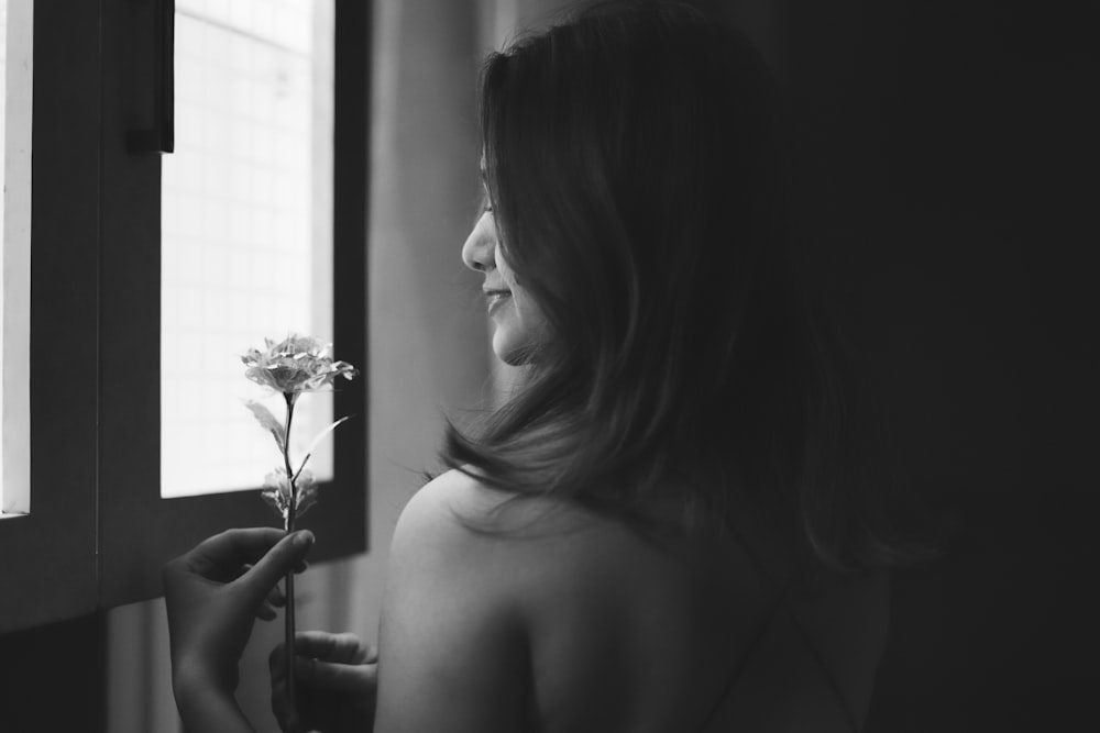 a woman holding a flower looking out a window