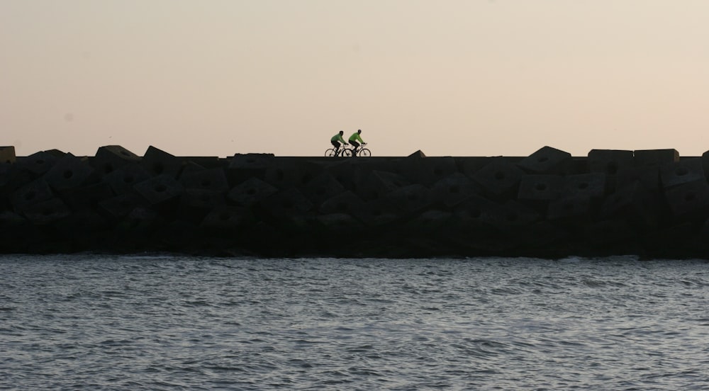 a couple of people riding bikes on top of a stone wall