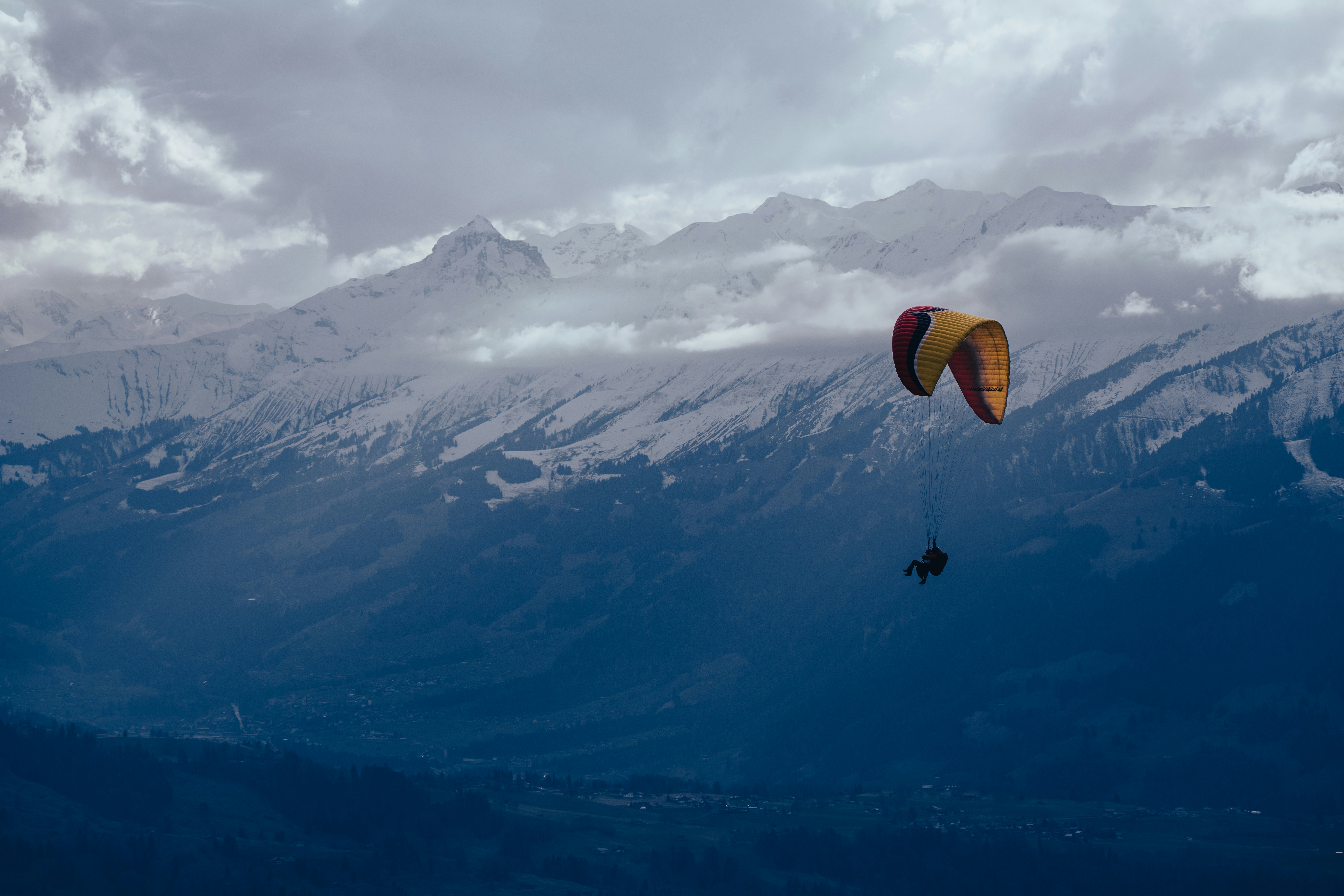 a person parasailing over a mountain range under a cloudy sky