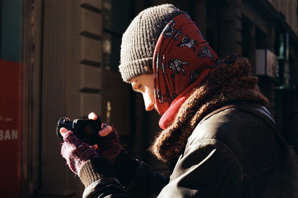 a woman wearing a hat and scarf is looking at her cell phone