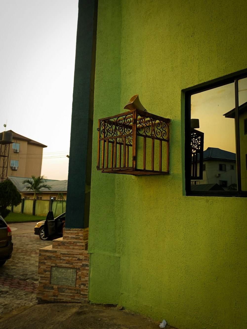 a green wall with a window and a birdcage on it