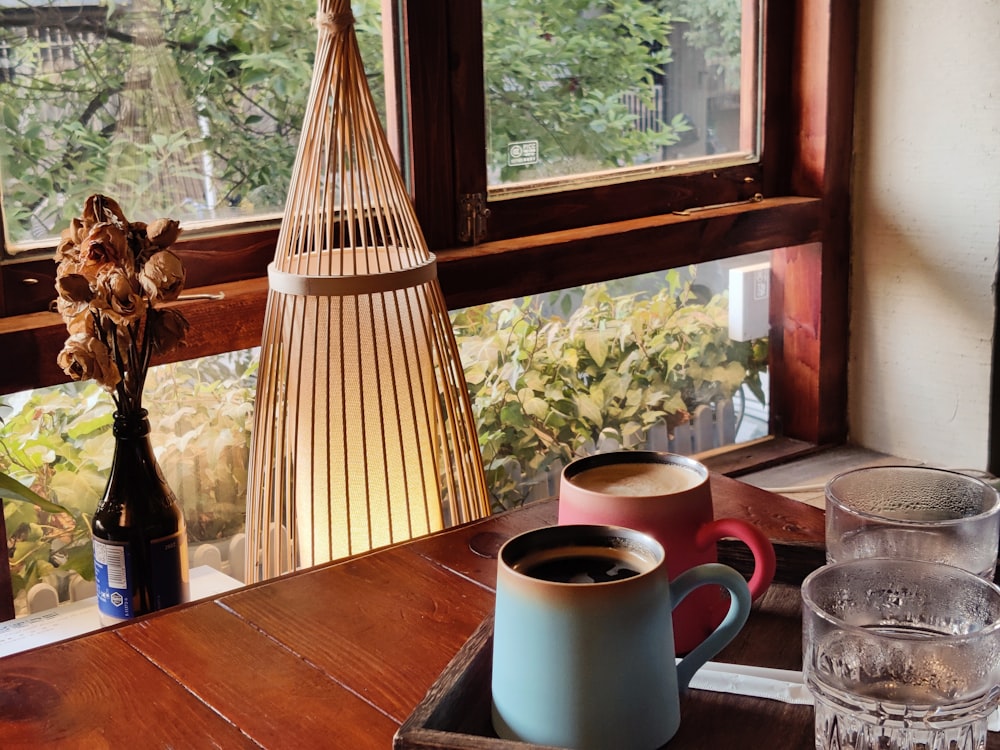 two cups of coffee sit on a tray in front of a window