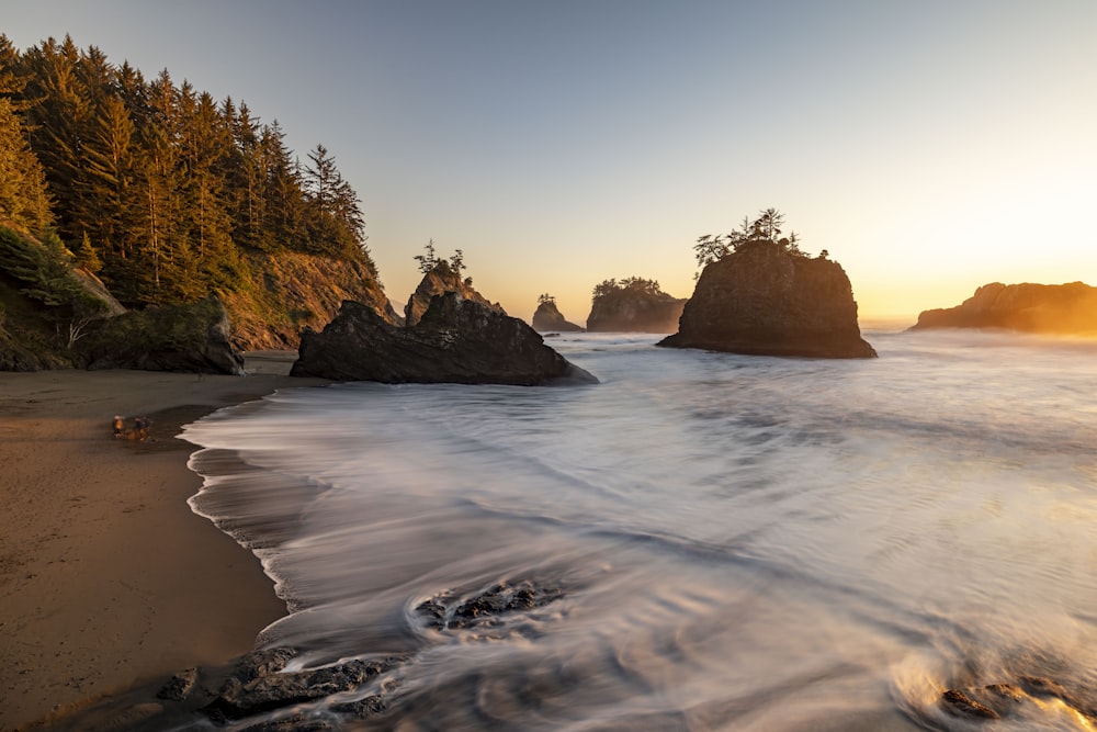 the sun is setting over the ocean with rocks in the foreground