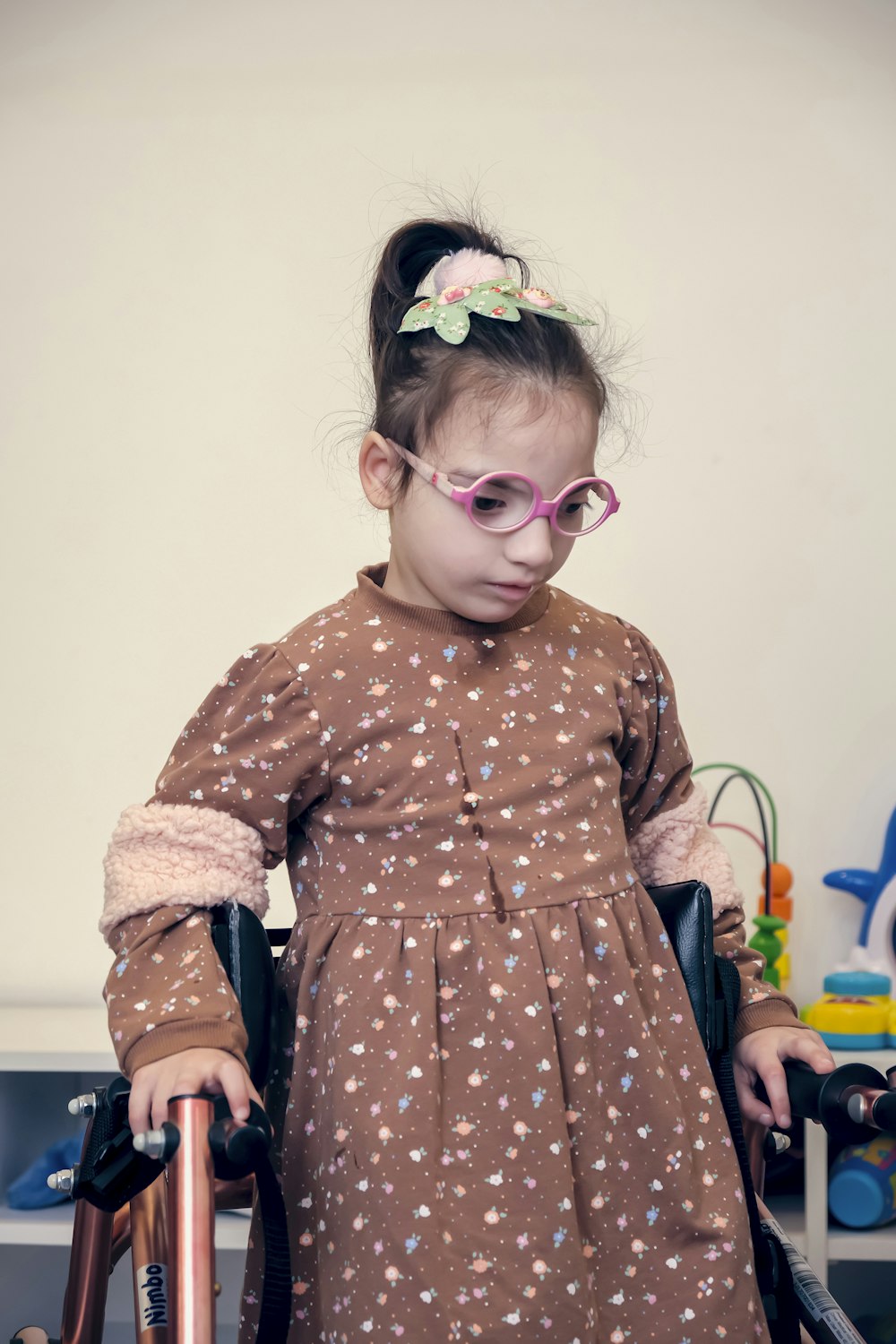 a little girl in a brown dress and pink glasses