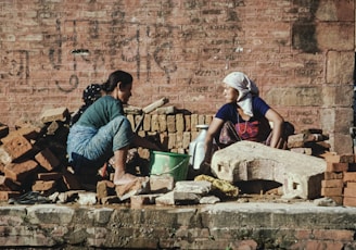 a couple of women sitting next to a pile of bricks