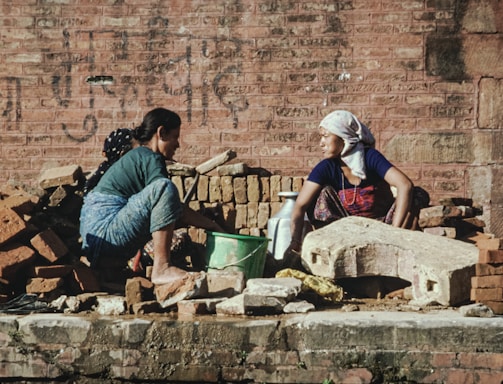 a couple of women sitting next to a pile of bricks