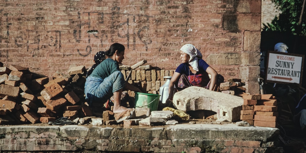 a couple of women sitting next to a pile of bricks