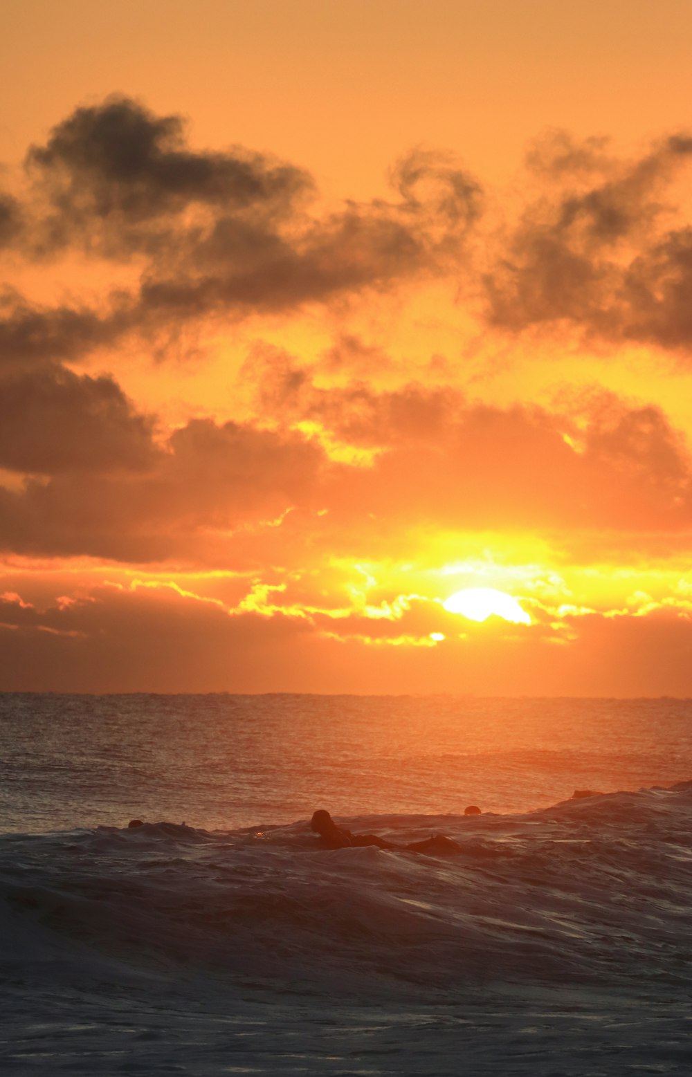 the sun is setting over the ocean with surfers in the water