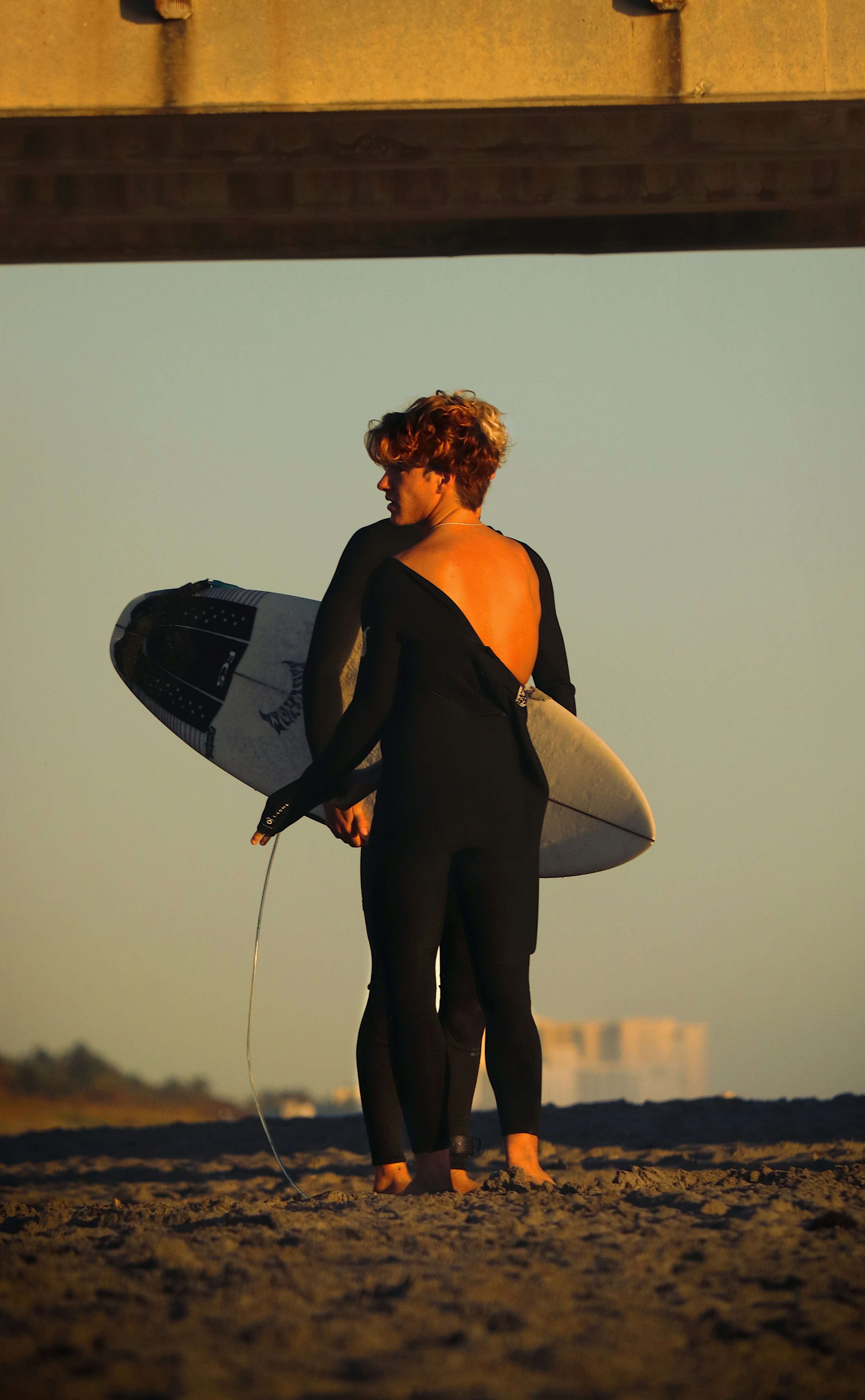 a woman holding a surfboard under a bridge