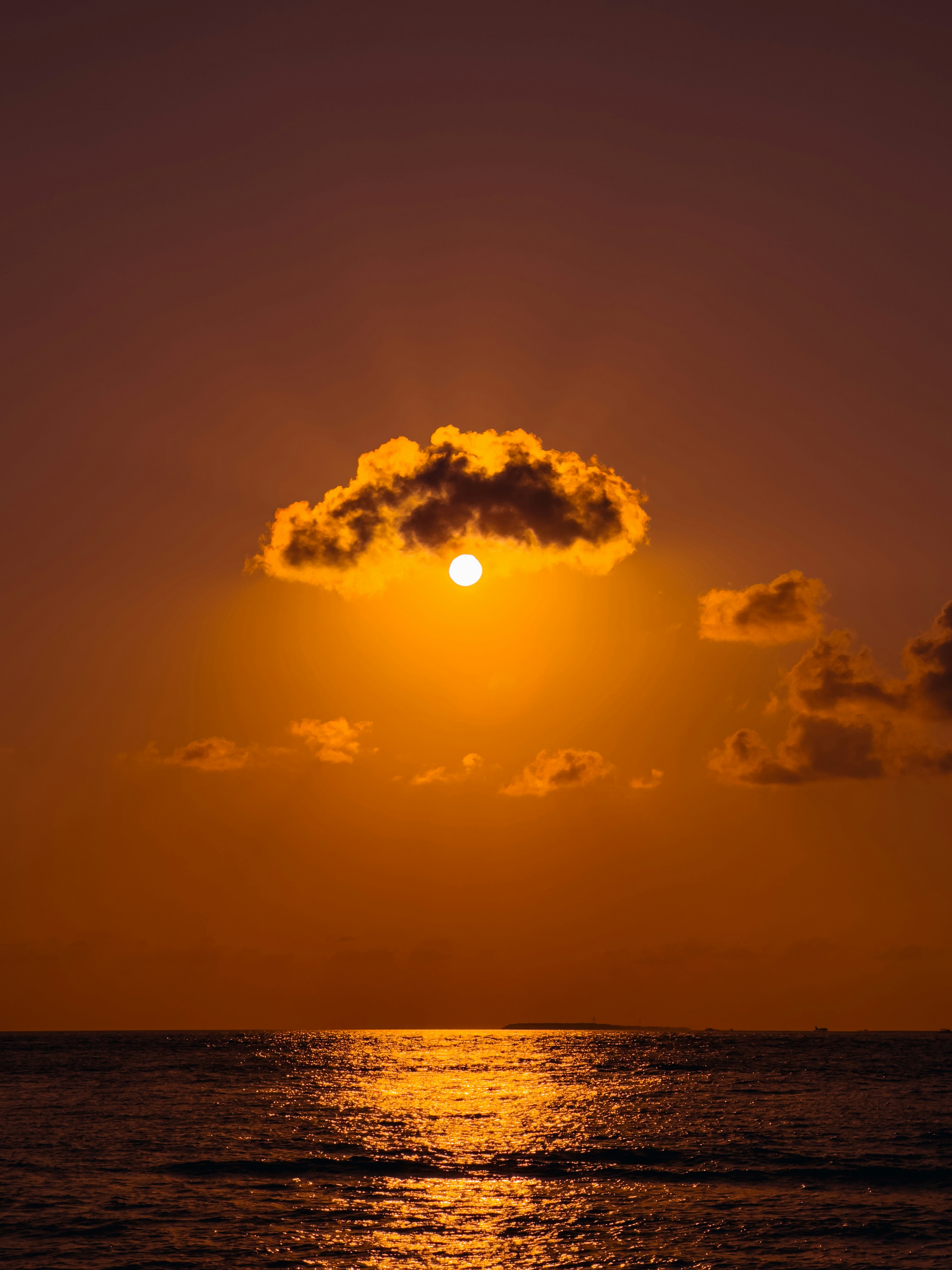 the sun setting over the ocean with a cloud in the sky