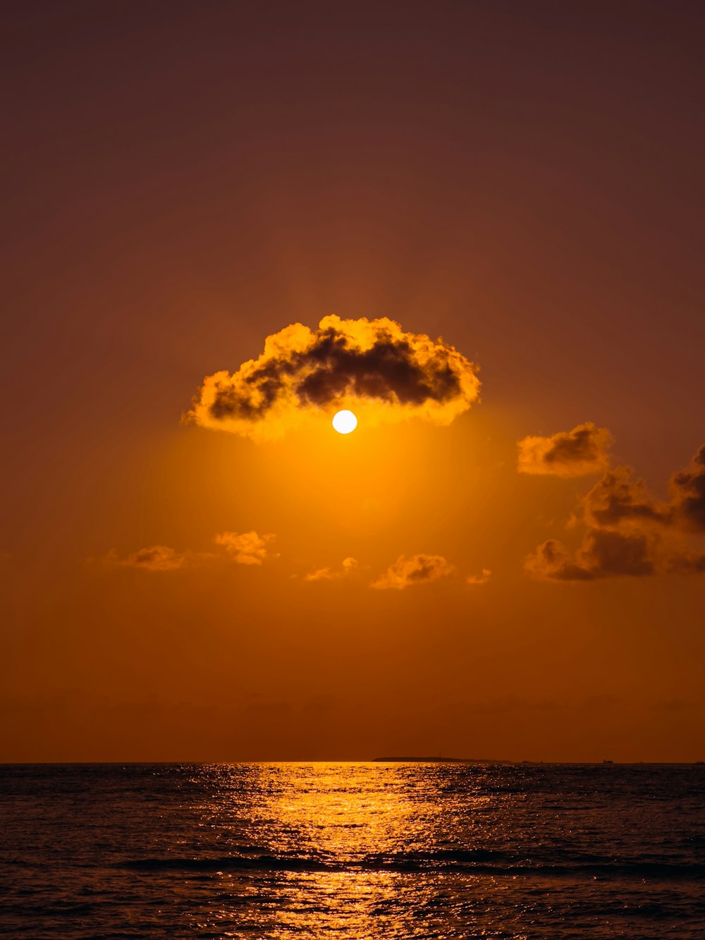 the sun setting over the ocean with a cloud in the sky