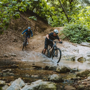 a couple of people riding bikes through a creek