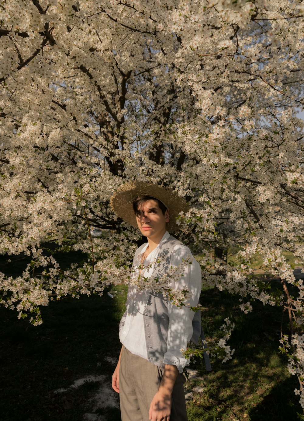 a man wearing a hat standing in front of a tree