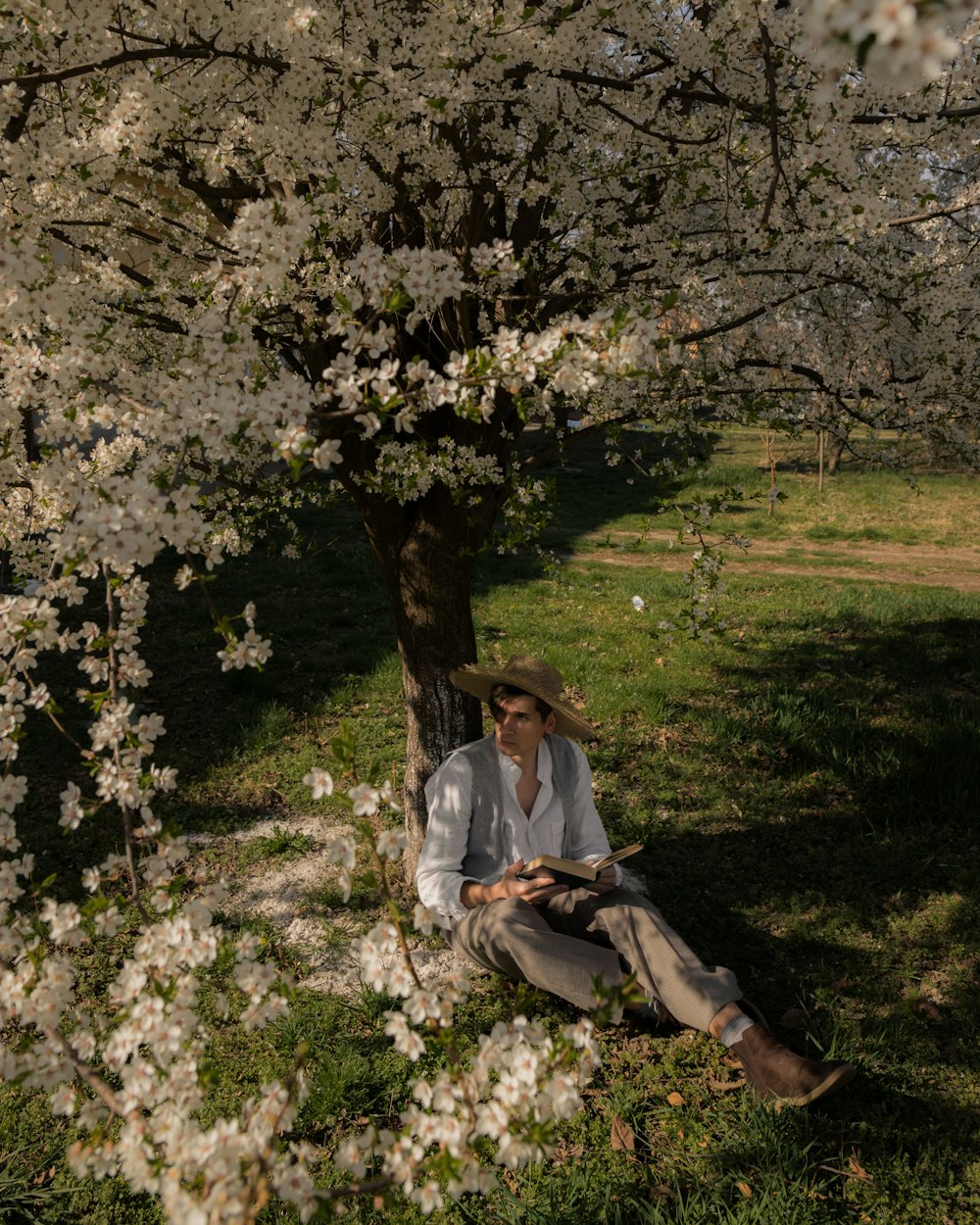 a man sitting under a tree with a hat on