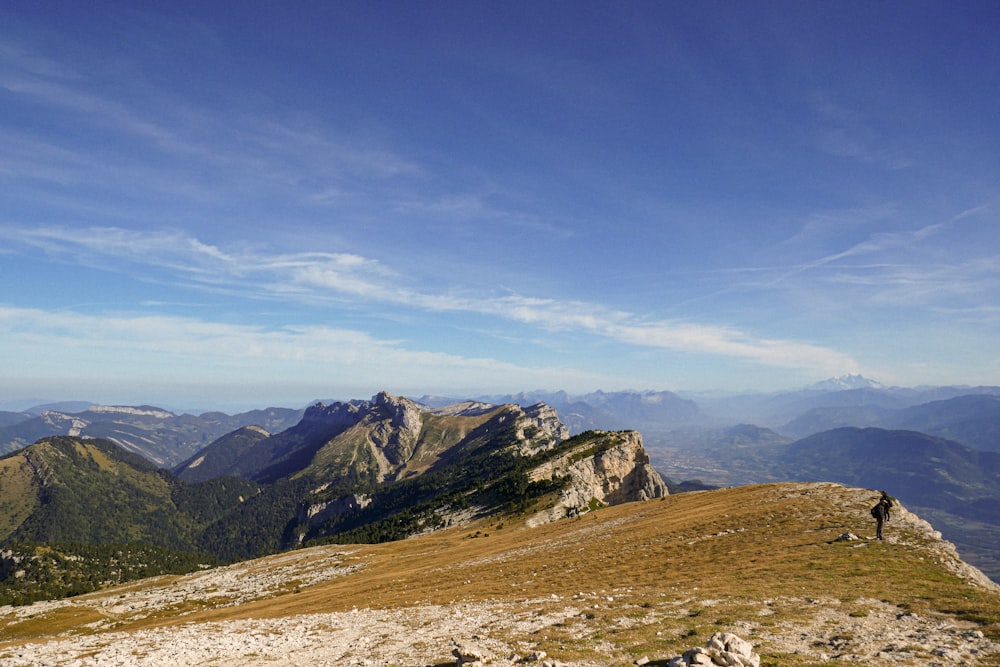 a man standing on top of a mountain next to a lush green hillside