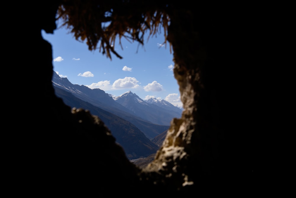 a view of a mountain range through a hole in a rock