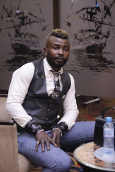 a man in a vest and tie sitting on a chair