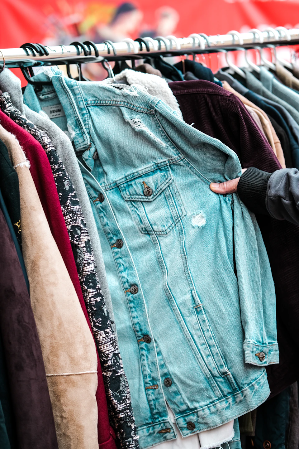 Tangan memegang jaket denim di rak