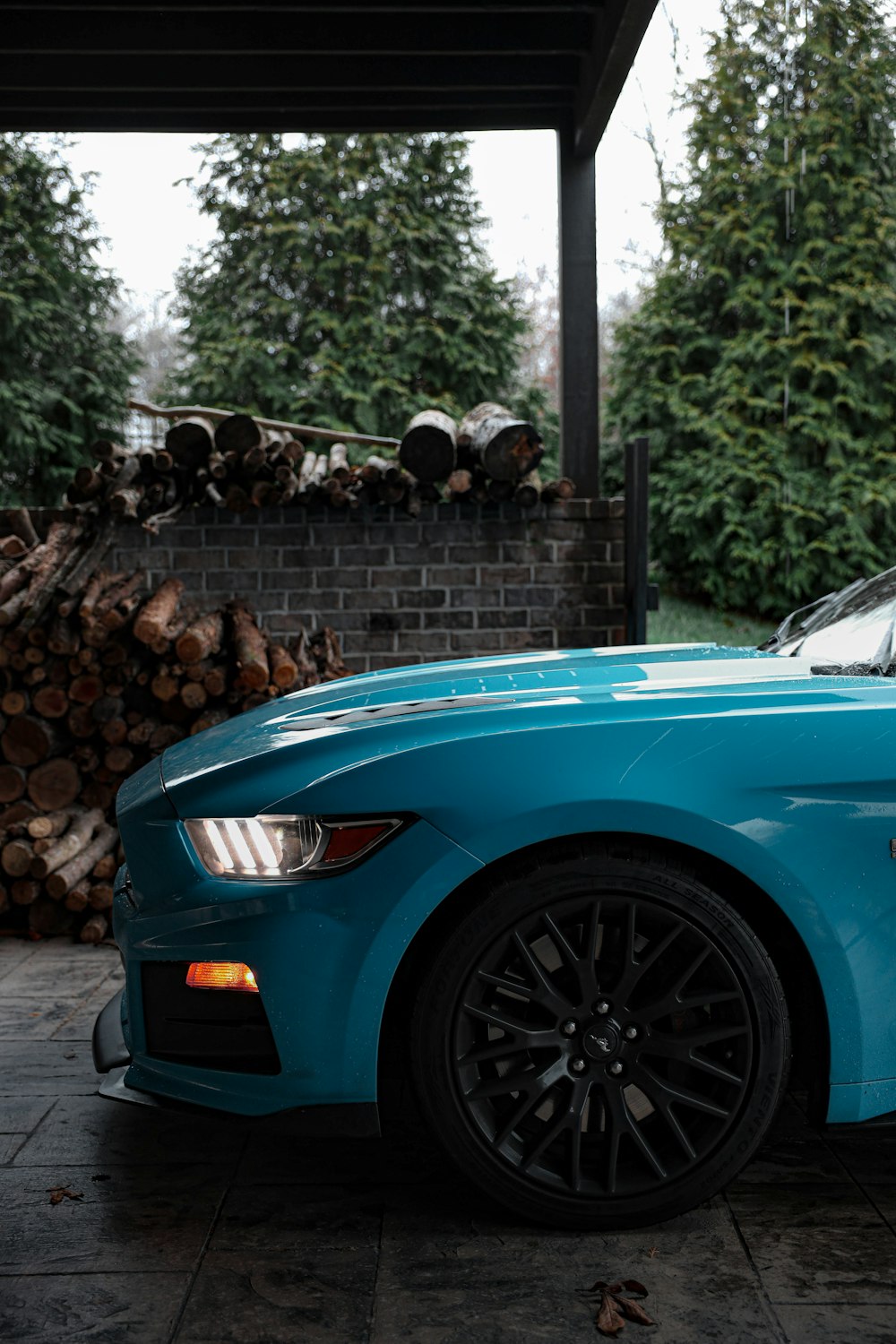 a blue car parked in front of a pile of logs