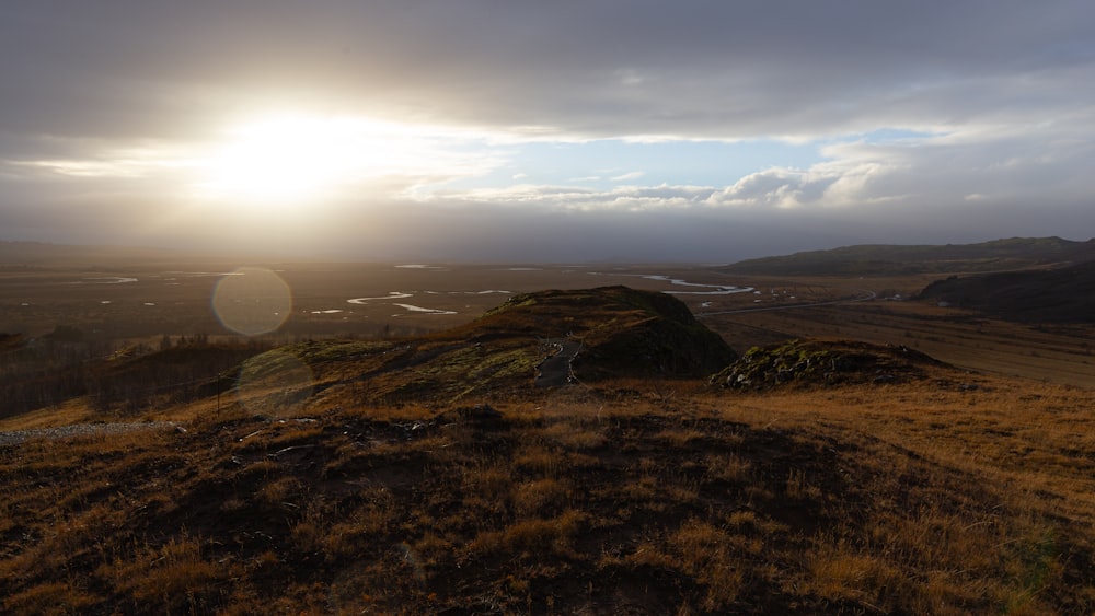 the sun is setting over a grassy hill