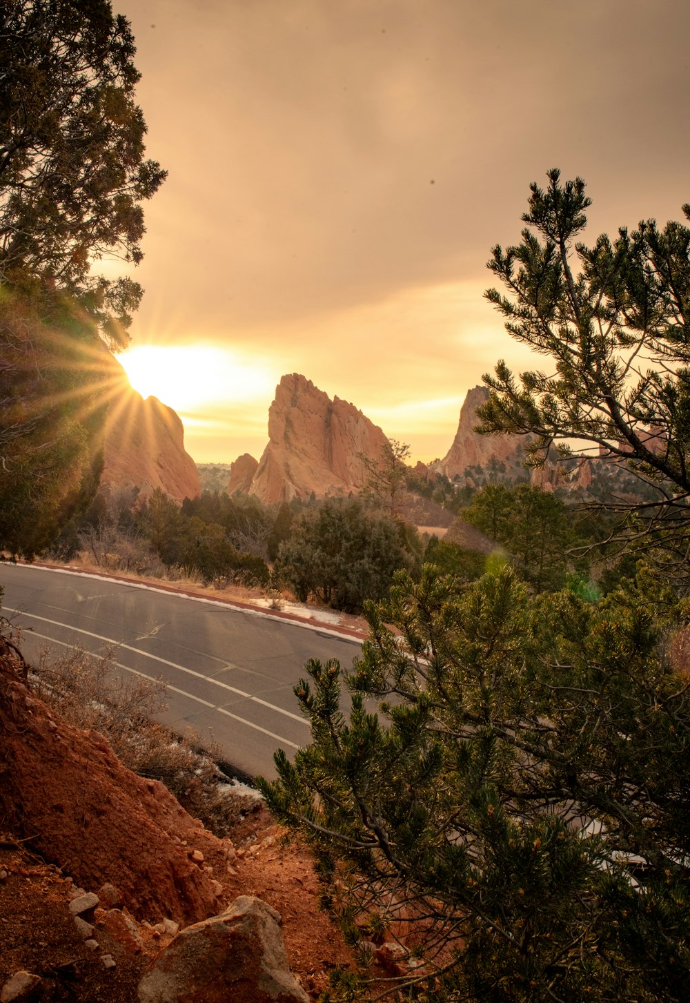 the sun is setting over a mountain road