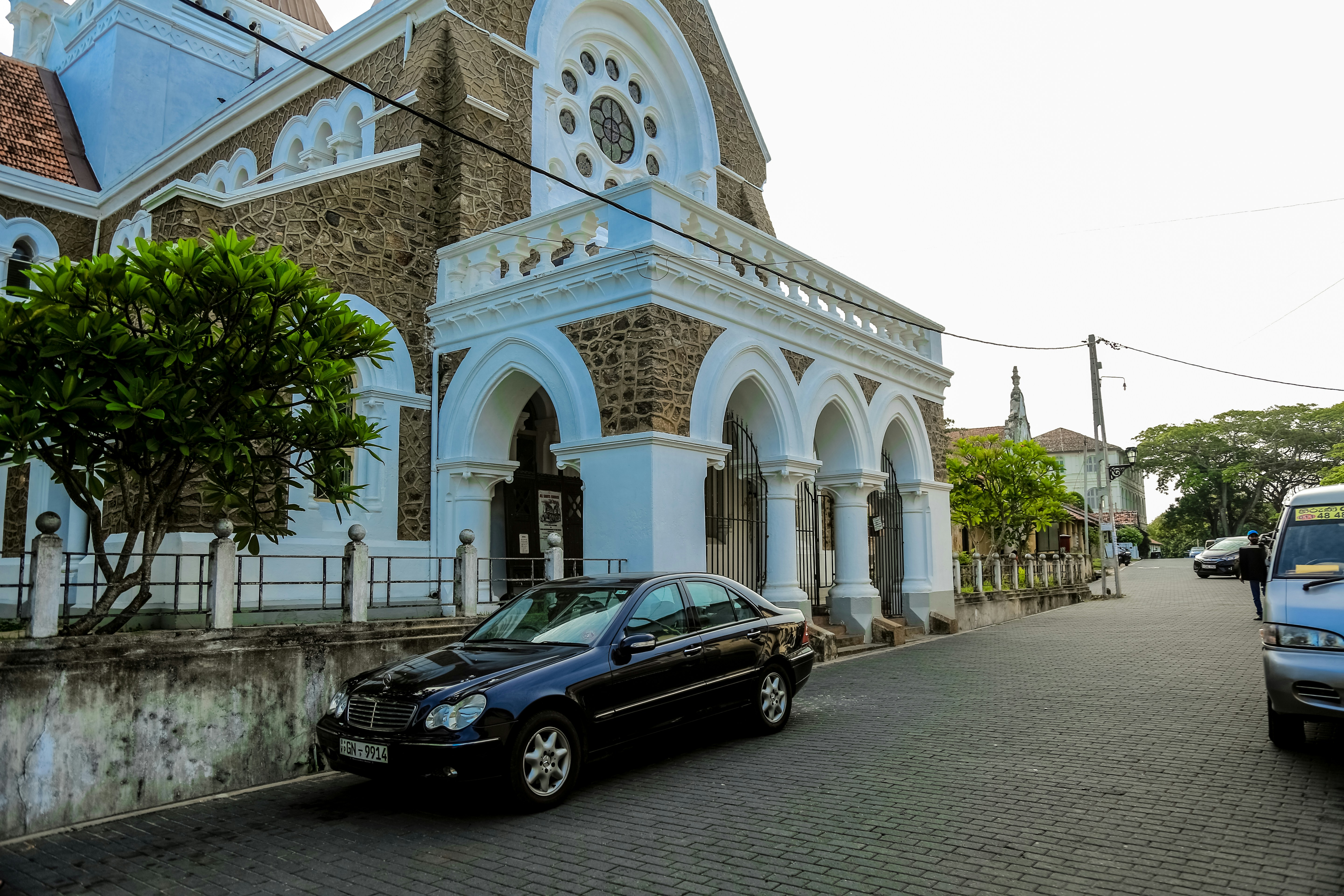 a black car parked in front of a church, A blue car parked in front of the church in Galle Fort.