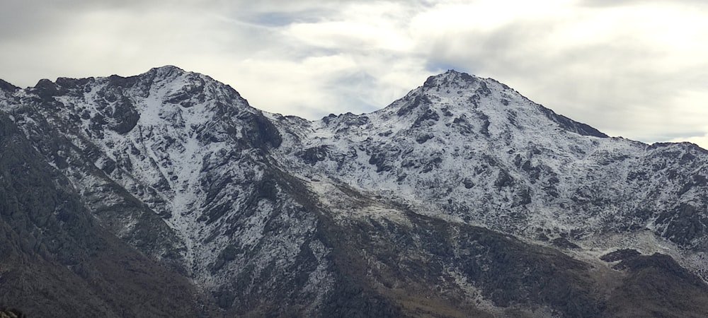 a mountain range covered in snow under a cloudy sky