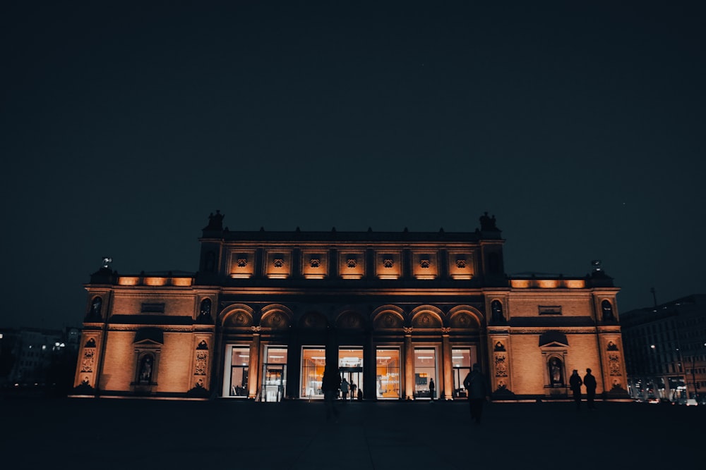 a building lit up at night with people standing outside