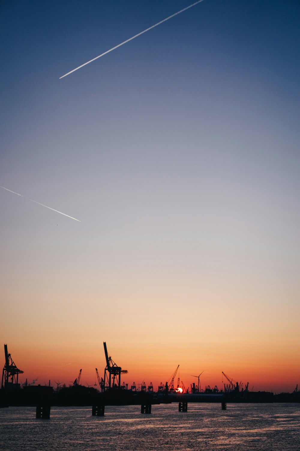 the sun is setting over a harbor with cranes