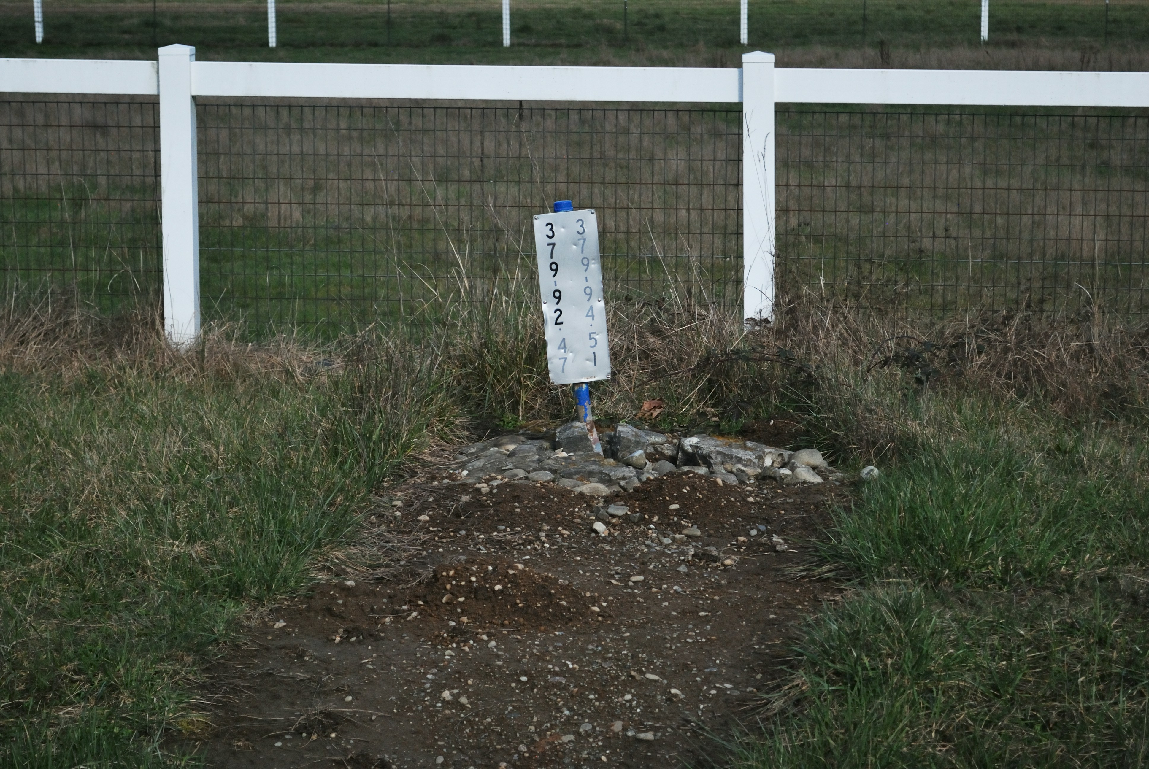 a sign in the middle of a field near a fence