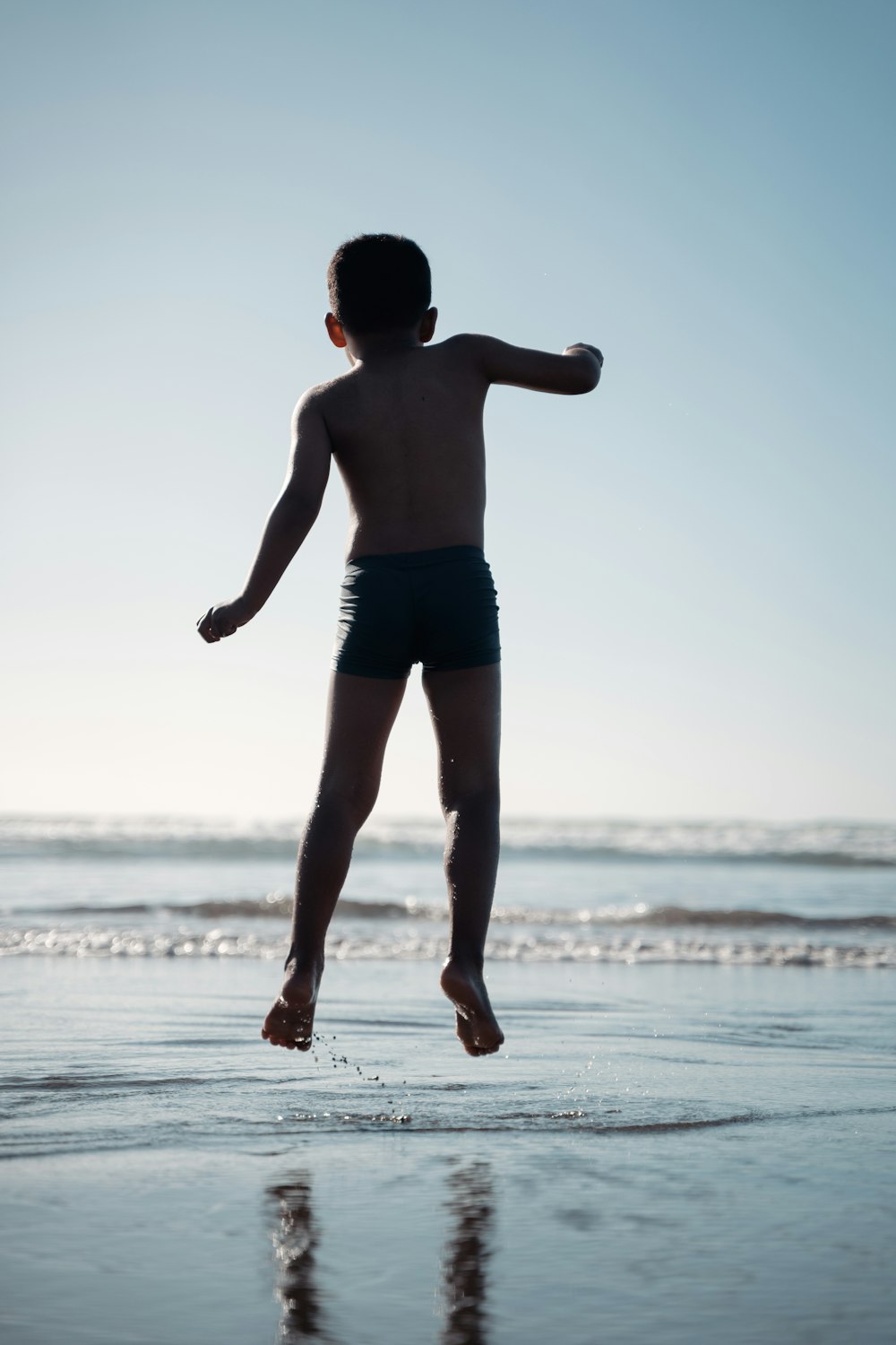 a young boy jumping into the air on a beach