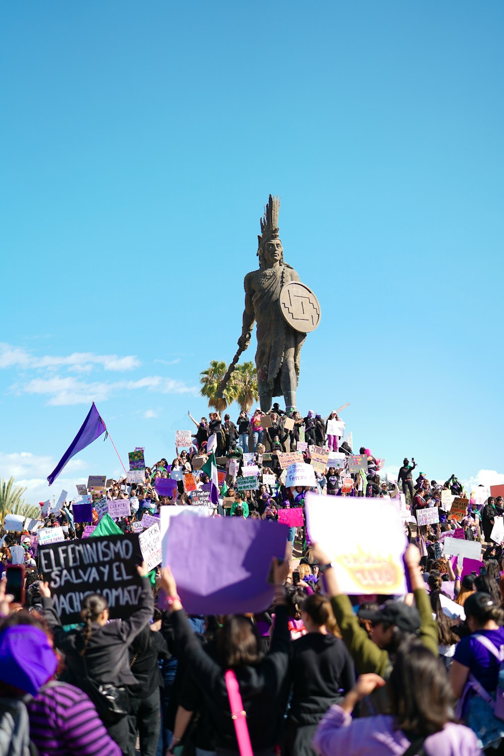a crowd of people holding signs in front of a statue
