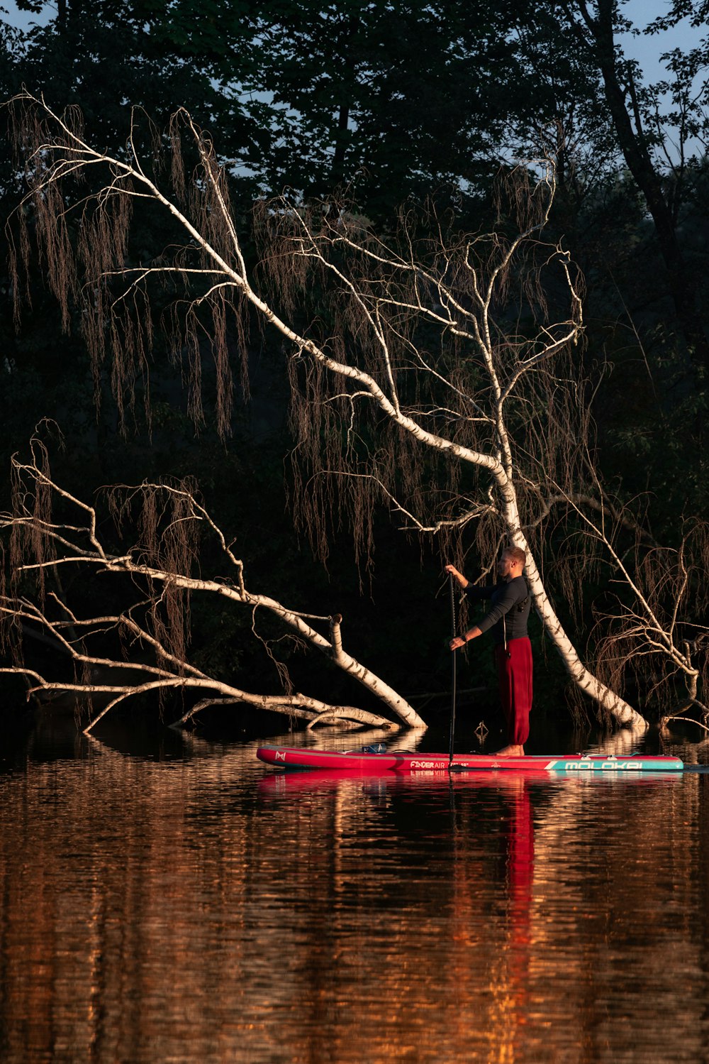 a man riding a red paddle board on top of a lake